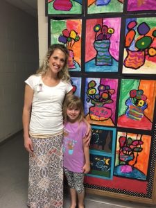 Wilkins Art Teacher Mrs. Hovden and a student pose in front of numerous pieces of student artwork